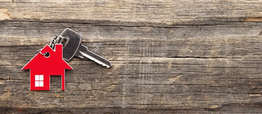 House key with red house-shaped keychain on a wooden background